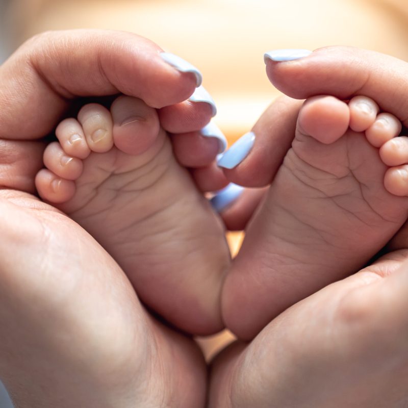 Mom holds the legs of a newborn baby in her hands, close-up, soft focus, concept of motherhood and care.